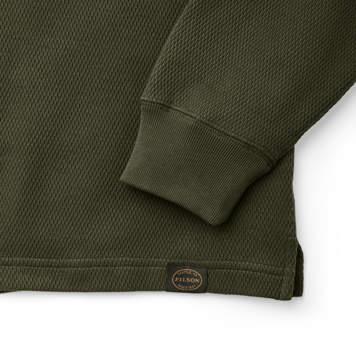Close-up of a green textured shirt with a visible Filson logo on a white background