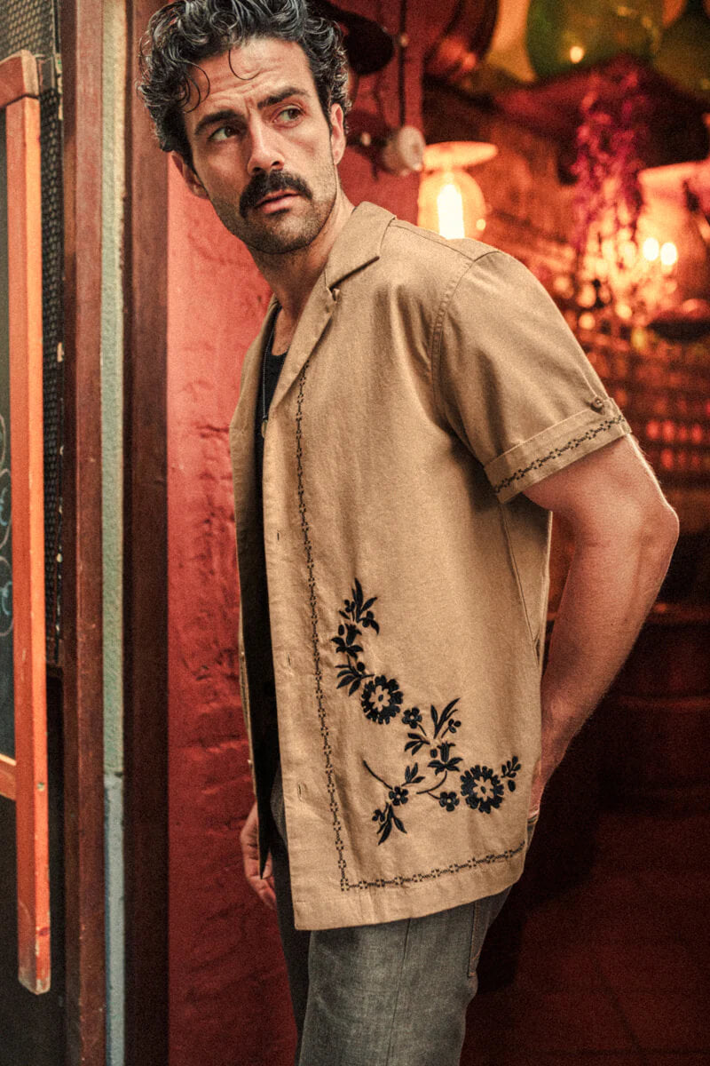 Man wearing a beige shirt with floral embroidery in a warm-toned interior setting