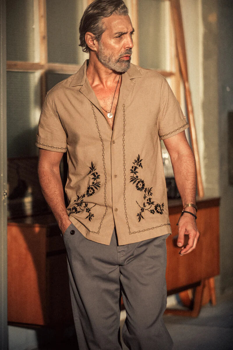 Man wearing a beige shirt with floral embroidery in an indoor setting