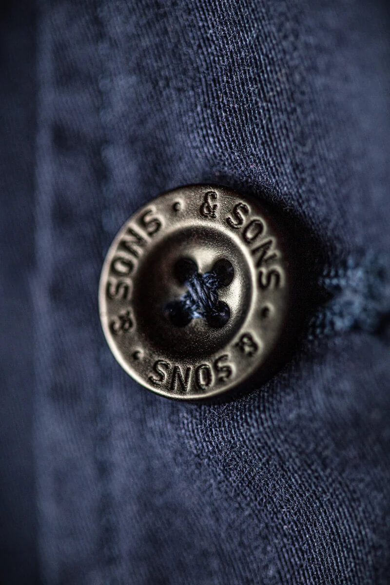 Close-up of a button with 'Sons & Sons' branding on a blue fabric background