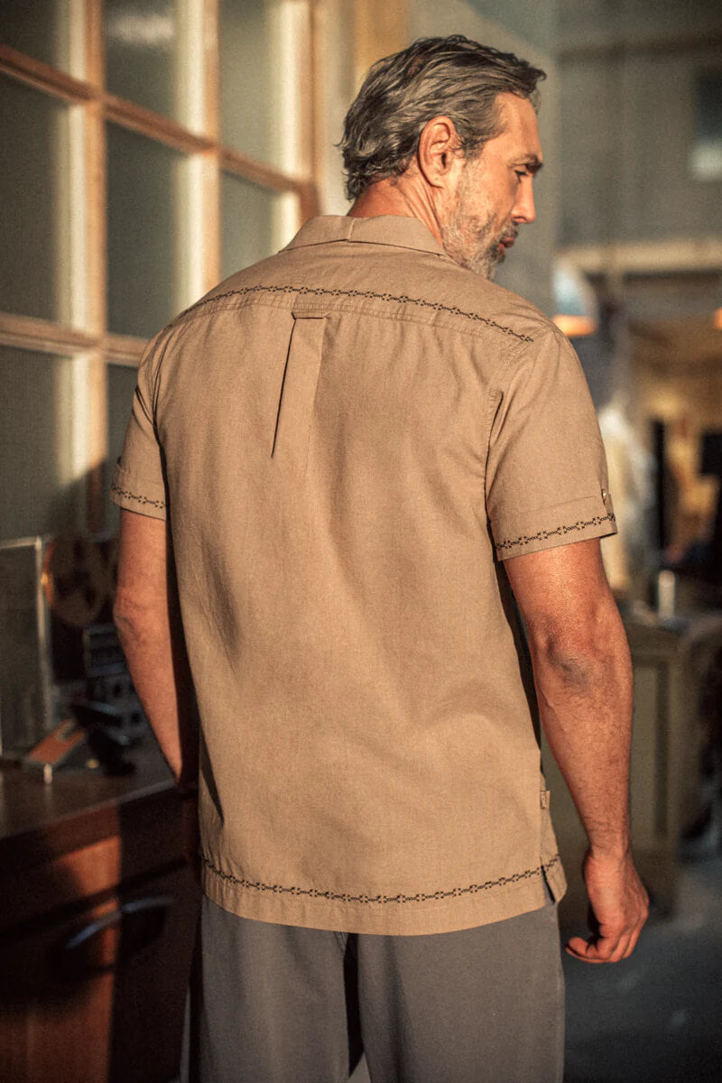 Man wearing a brown shirt with intricate stitching in an indoor setting