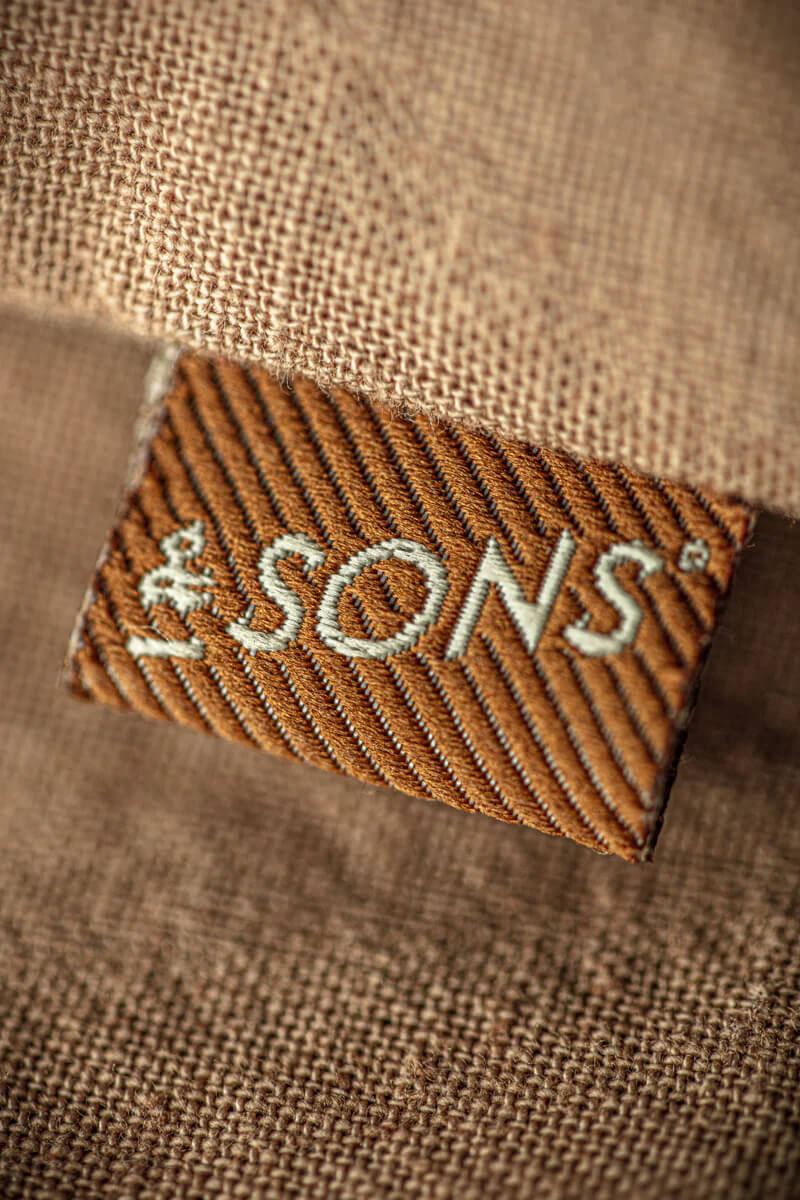 Close-up of a woven label with '&Sons' on a brown fabric background