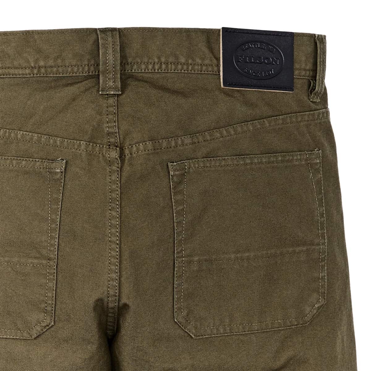 Close-up of the back waistband and pockets of olive green denim shorts, featuring a black leather patch with the brand name 'FILSON'.