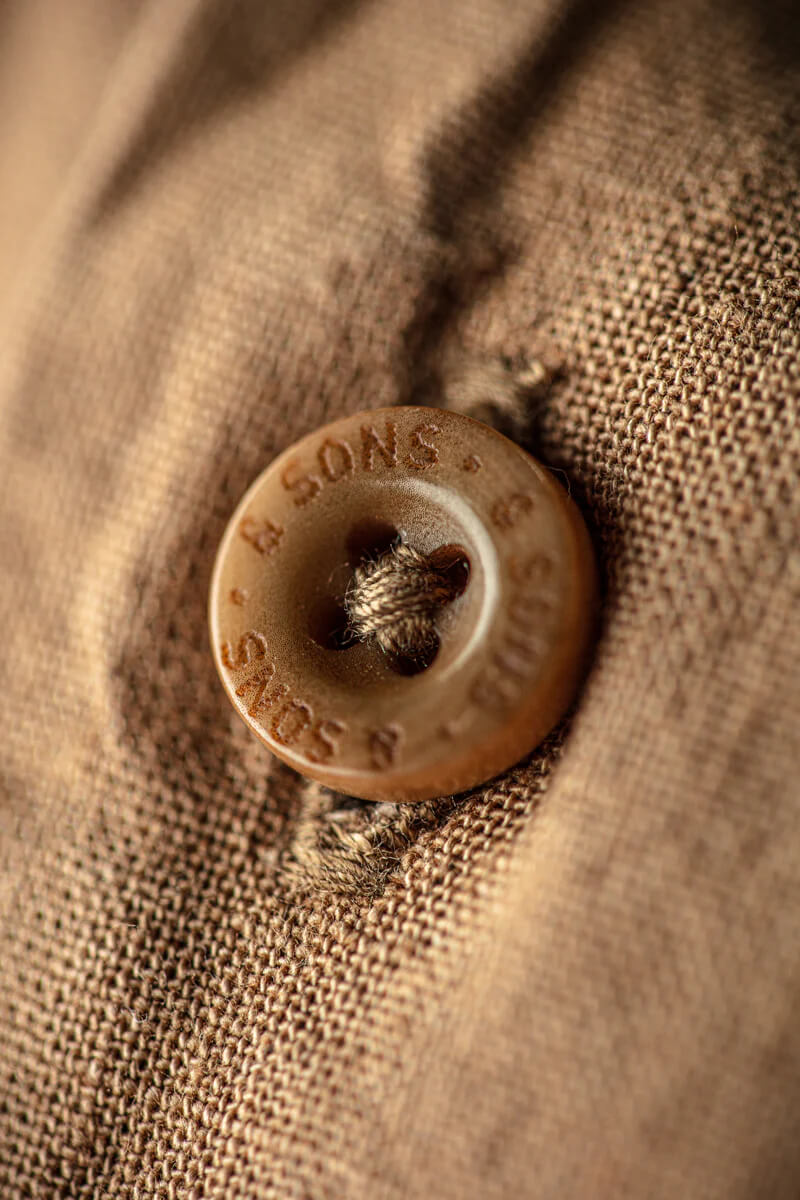 Close-up of a button on brown fabric with '& SONS' branding.