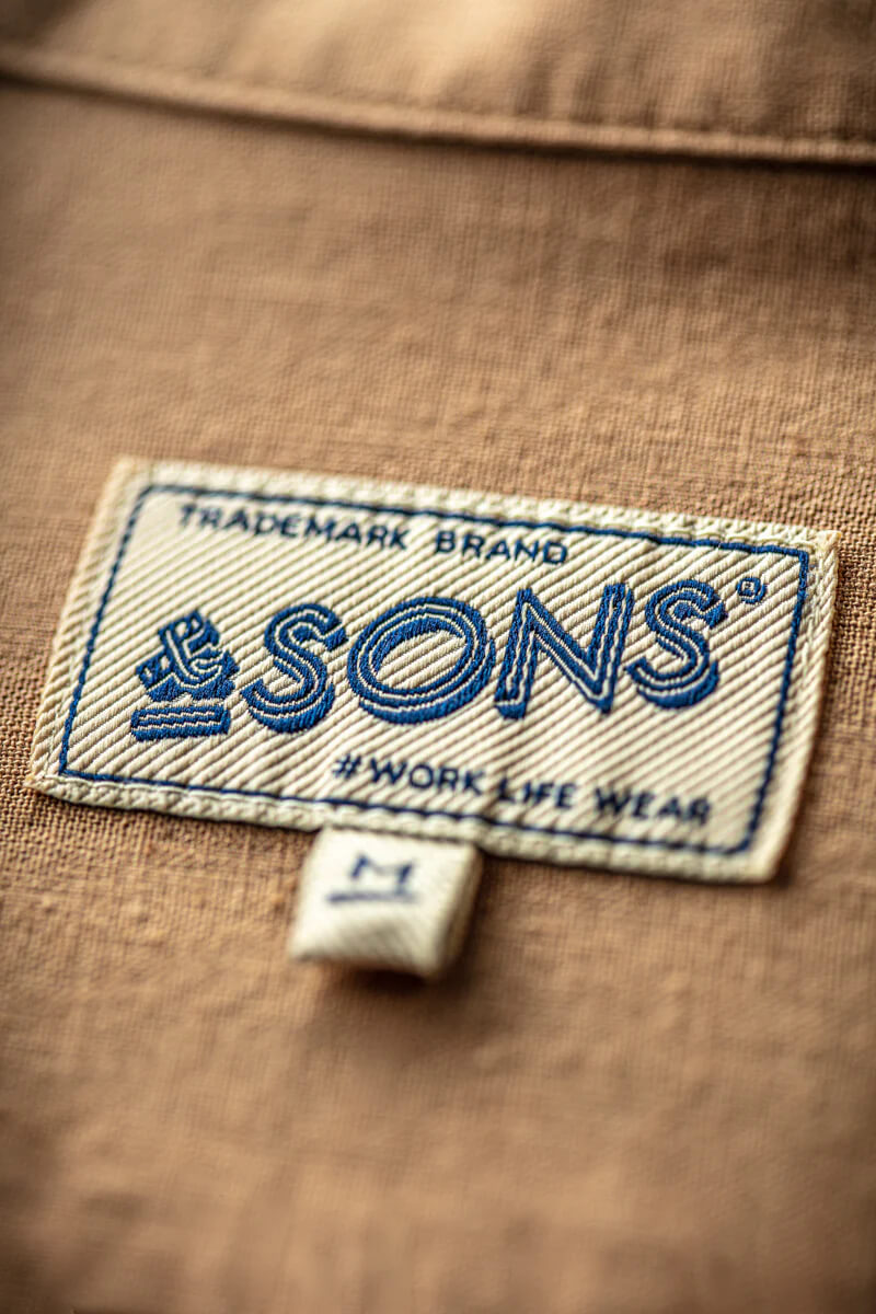 Close-up of a '&SONS' brand label on brown fabric