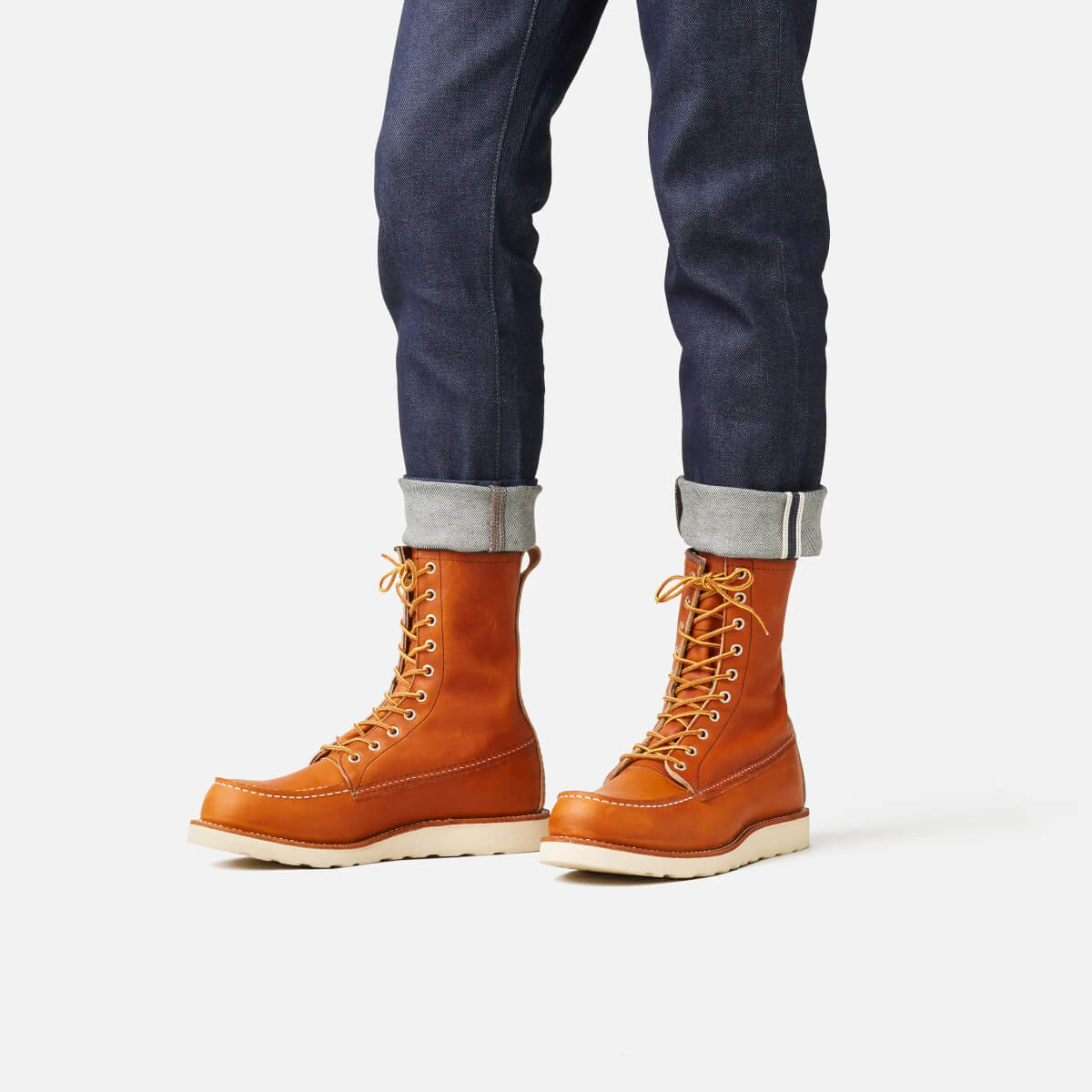 Brown leather boots worn with dark blue jeans on a white background
