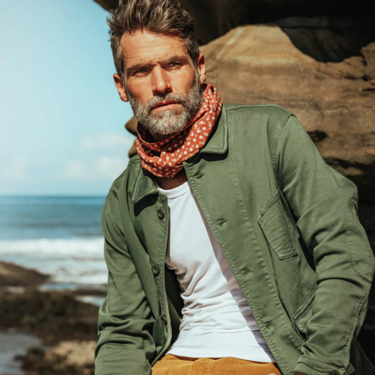Man wearing a green jacket and red patterned scarf by the ocean