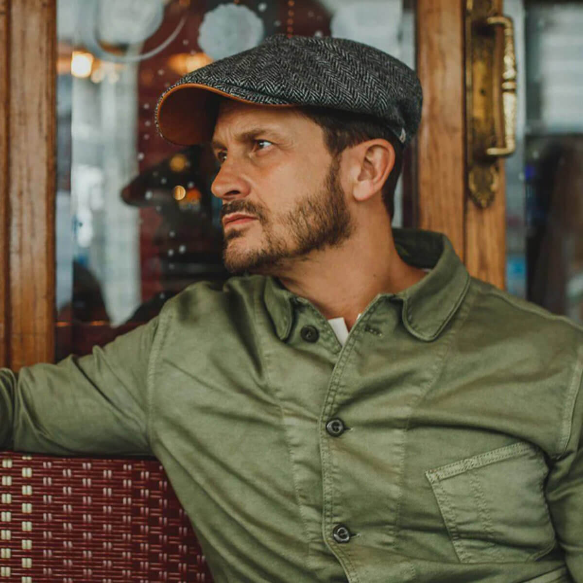 Man wearing a green jacket and cap in an indoor setting