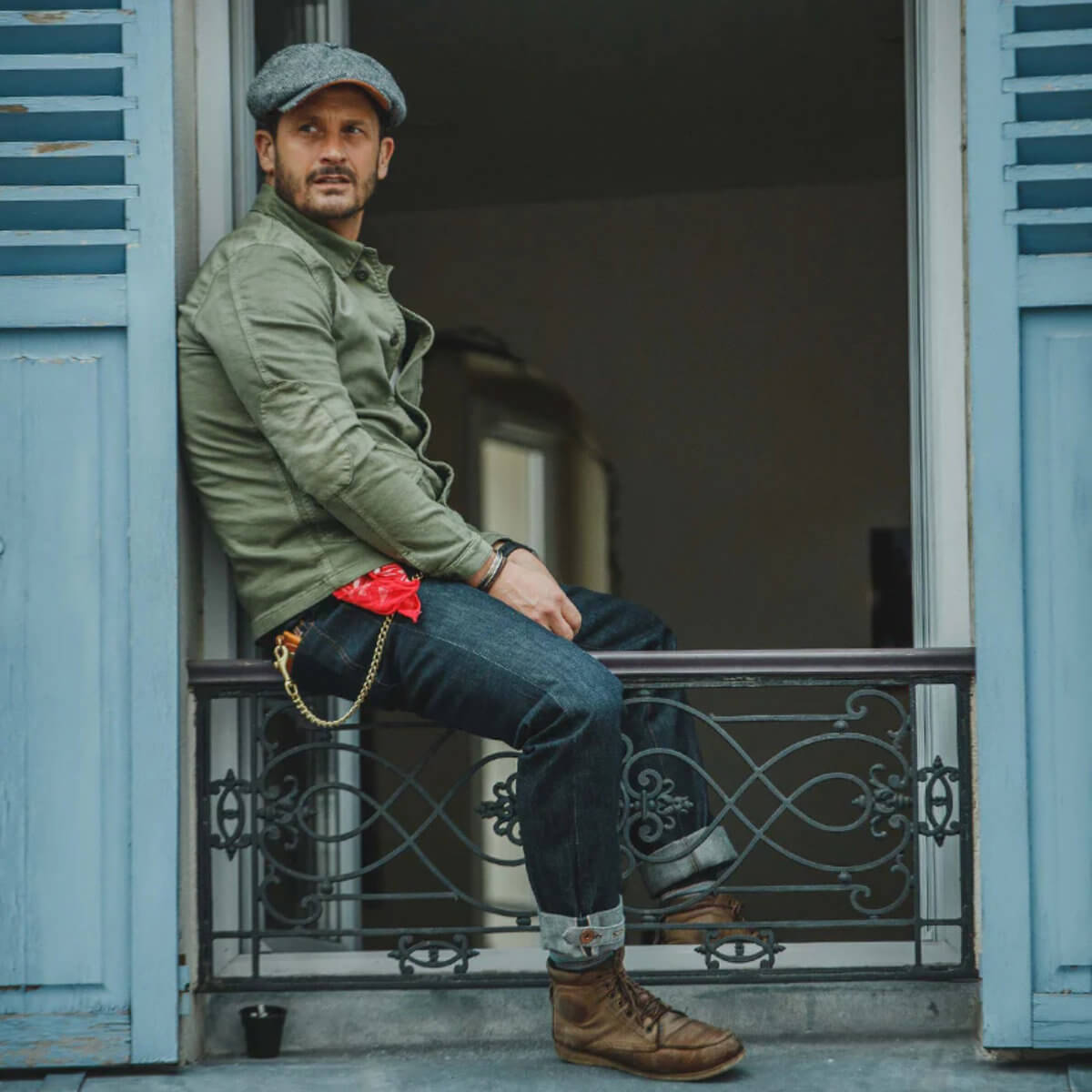 Man sitting on a balcony with a green jacket and brown boots.