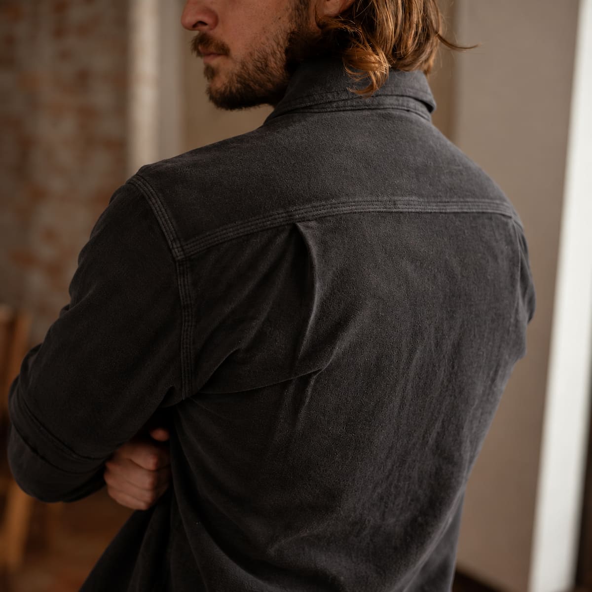 A man wearing an Iron and Resin Journeyman Moleskin Shirt, shown from the back in a softly lit indoor setting.
