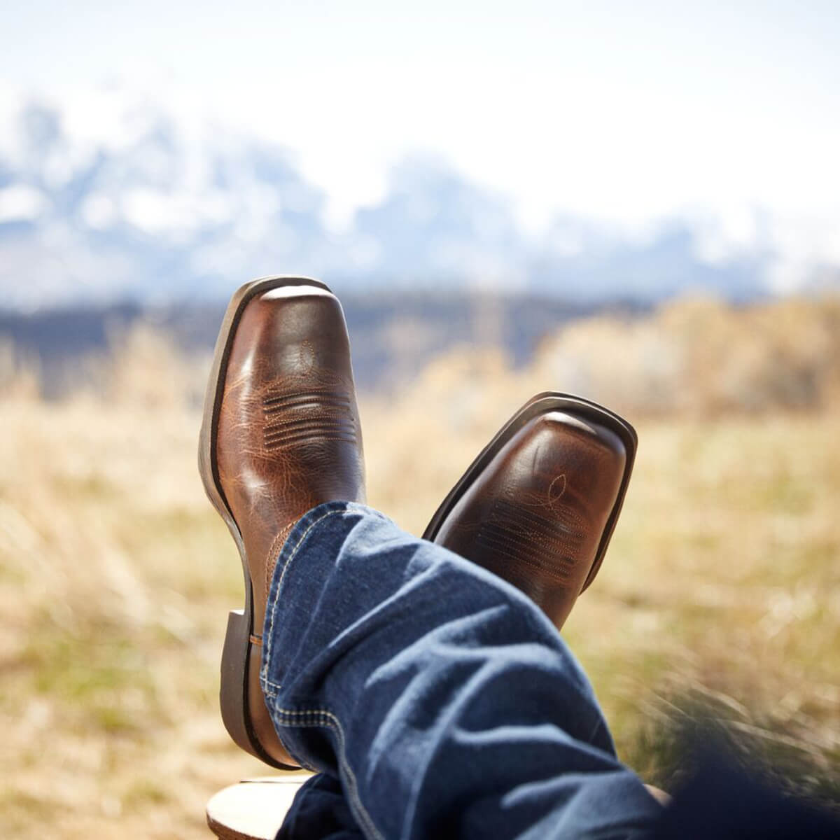 Brown leather boots and blue jeans with a blurred natural background