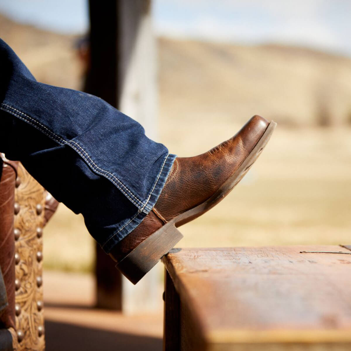 Brown leather boot and blue jeans on a blurred outdoor background