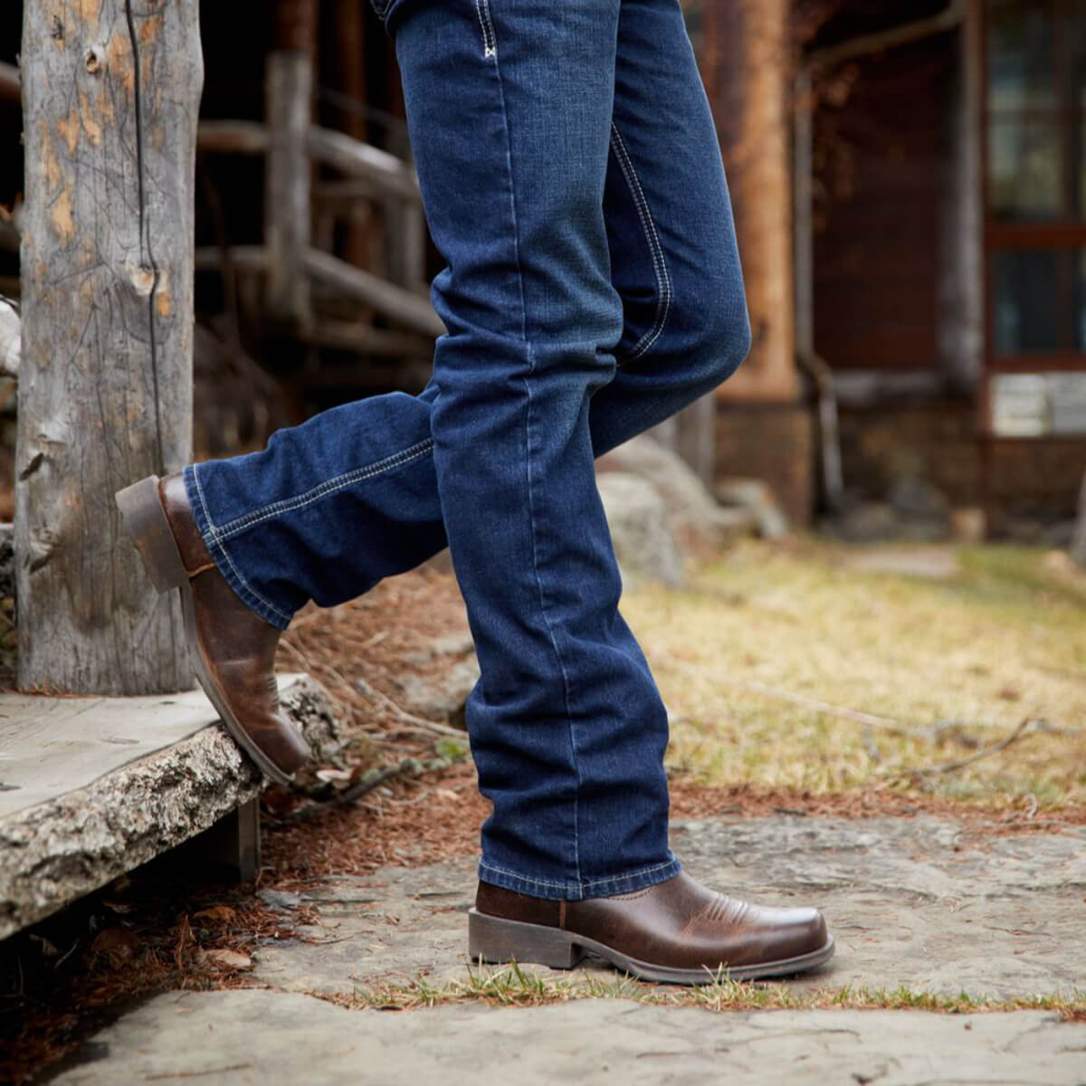 Person wearing blue jeans and brown boots stepping onto a wooden platform.