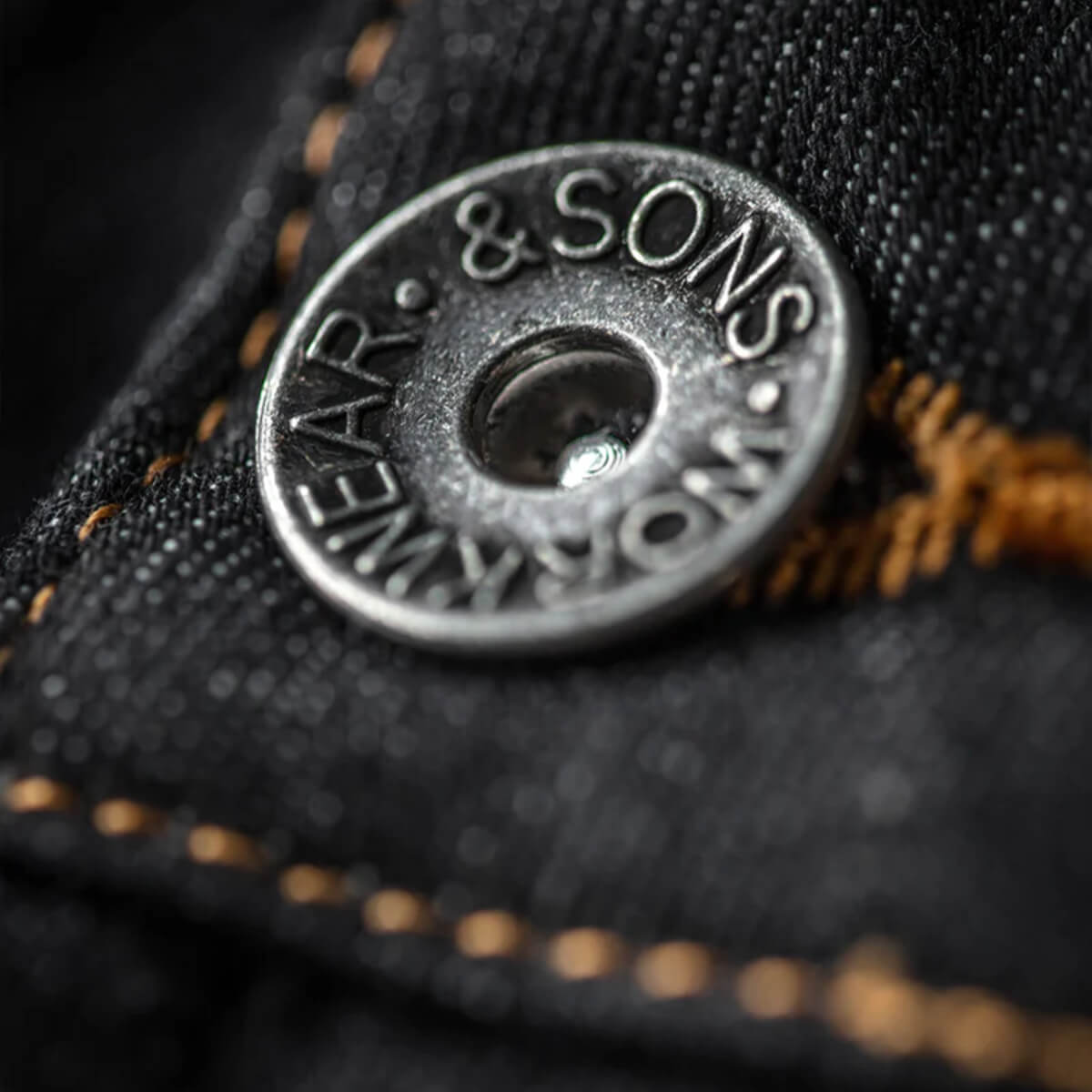 Close-up of a button with &amp;Sons branding on black fabric.
