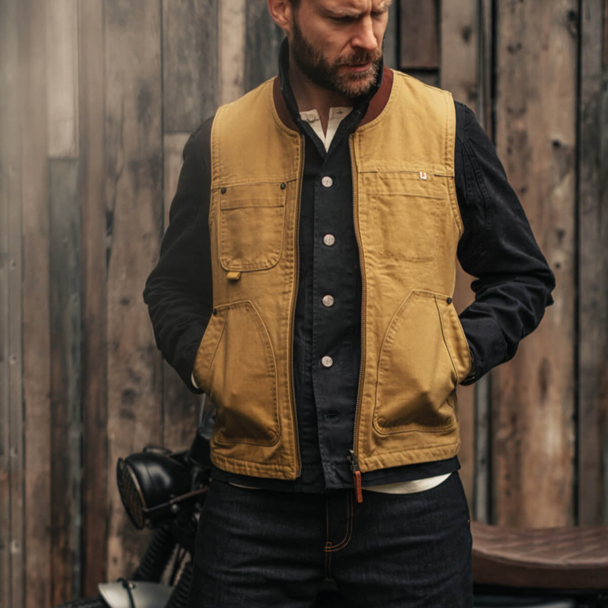 Man wearing a mustard yellow vest over a black shirt against a wooden background