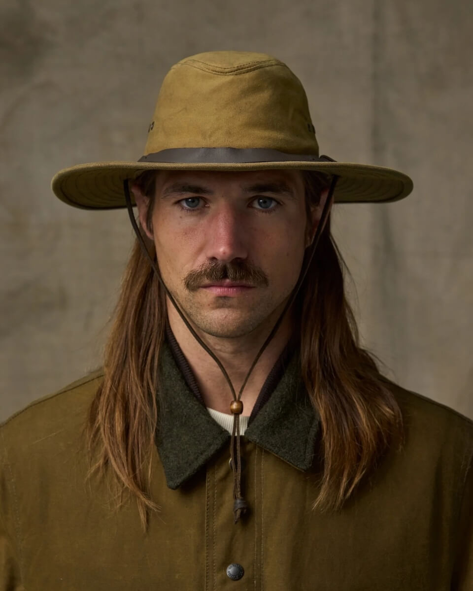 Man wearing a wide-brimmed Filson Bush hat and brown jacket against a neutral background
