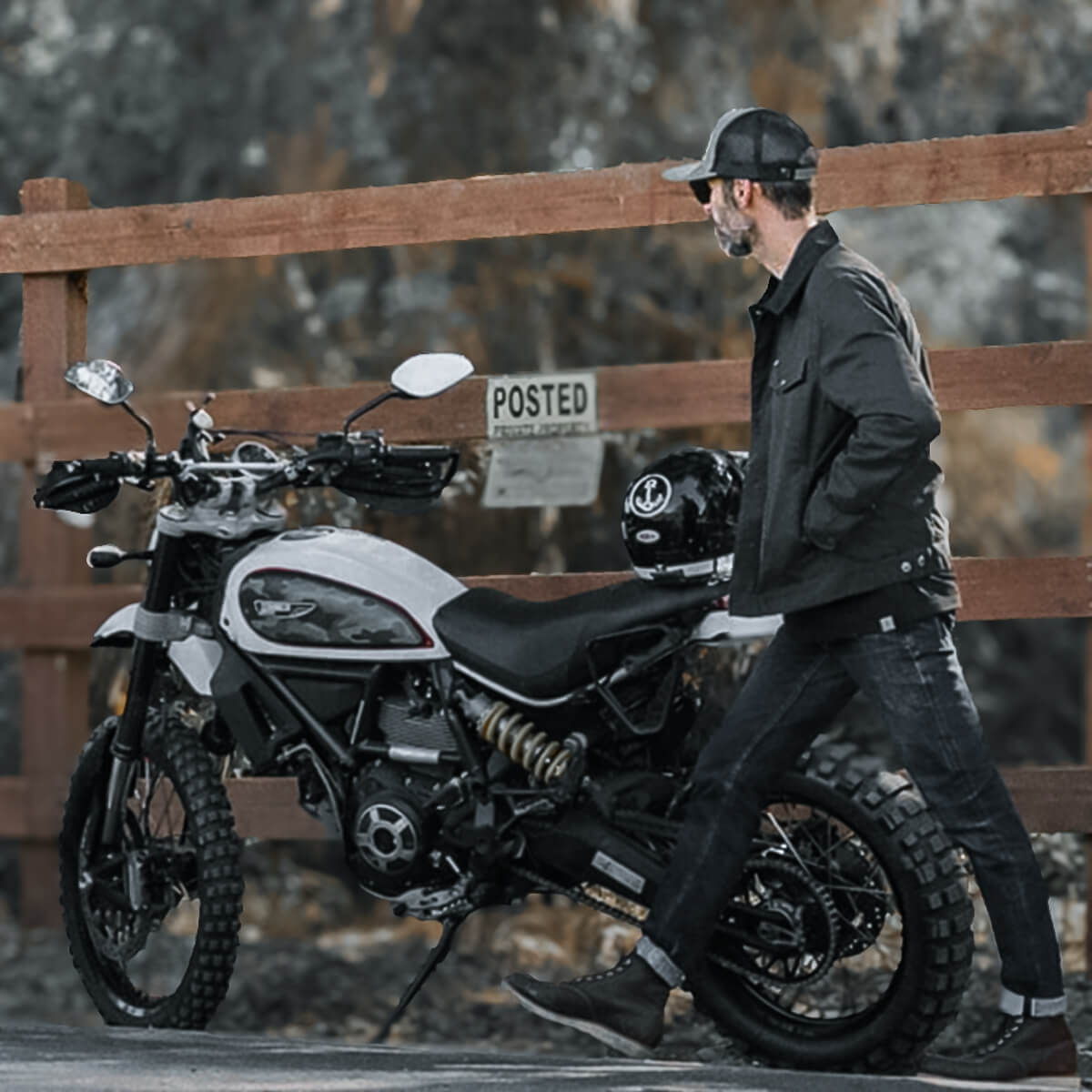 Man standing next to a motorcycle with a helmet on a wooden fence background
