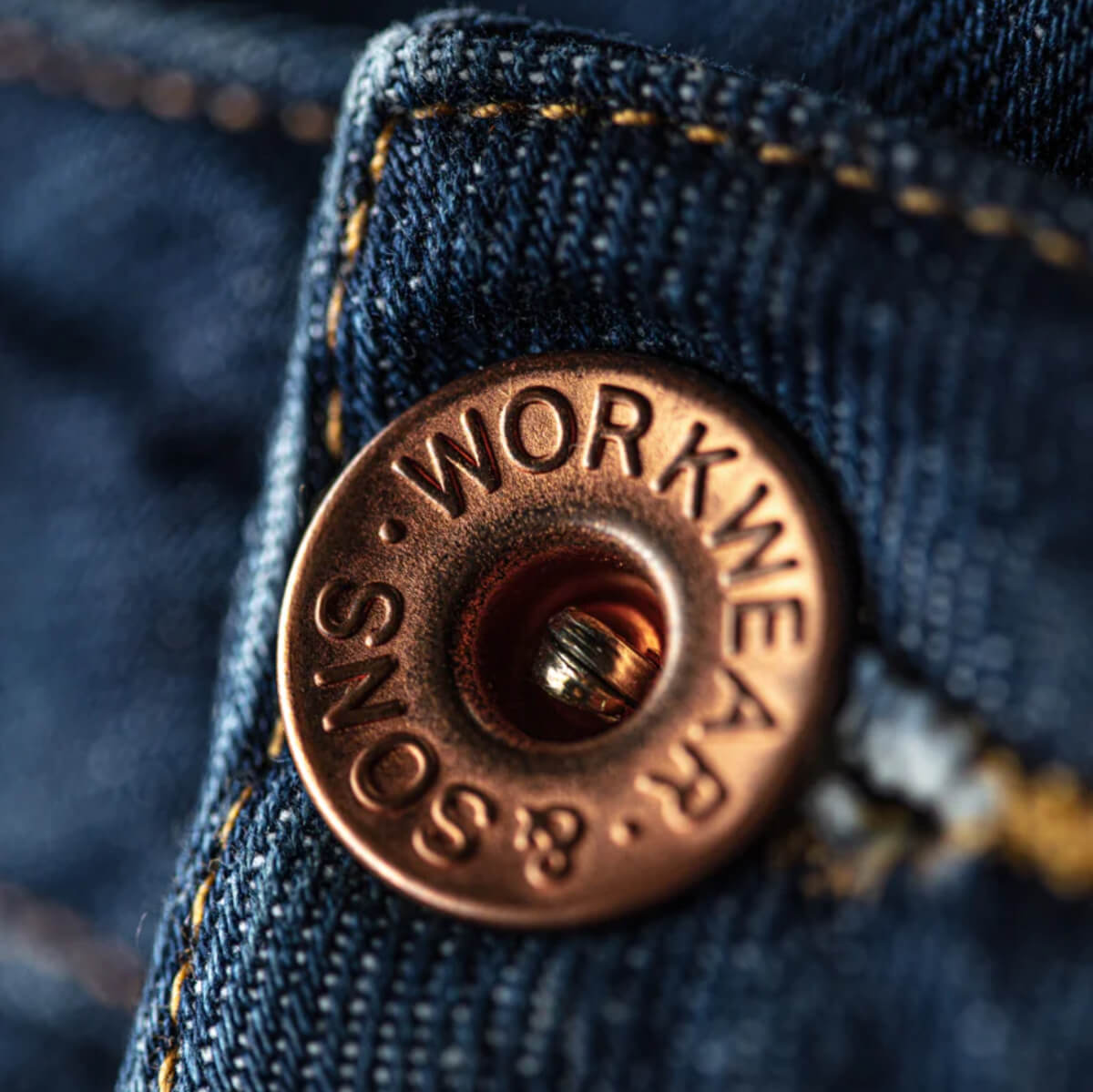 Close-up of a button on blue denim fabric with 'Workne' branding.