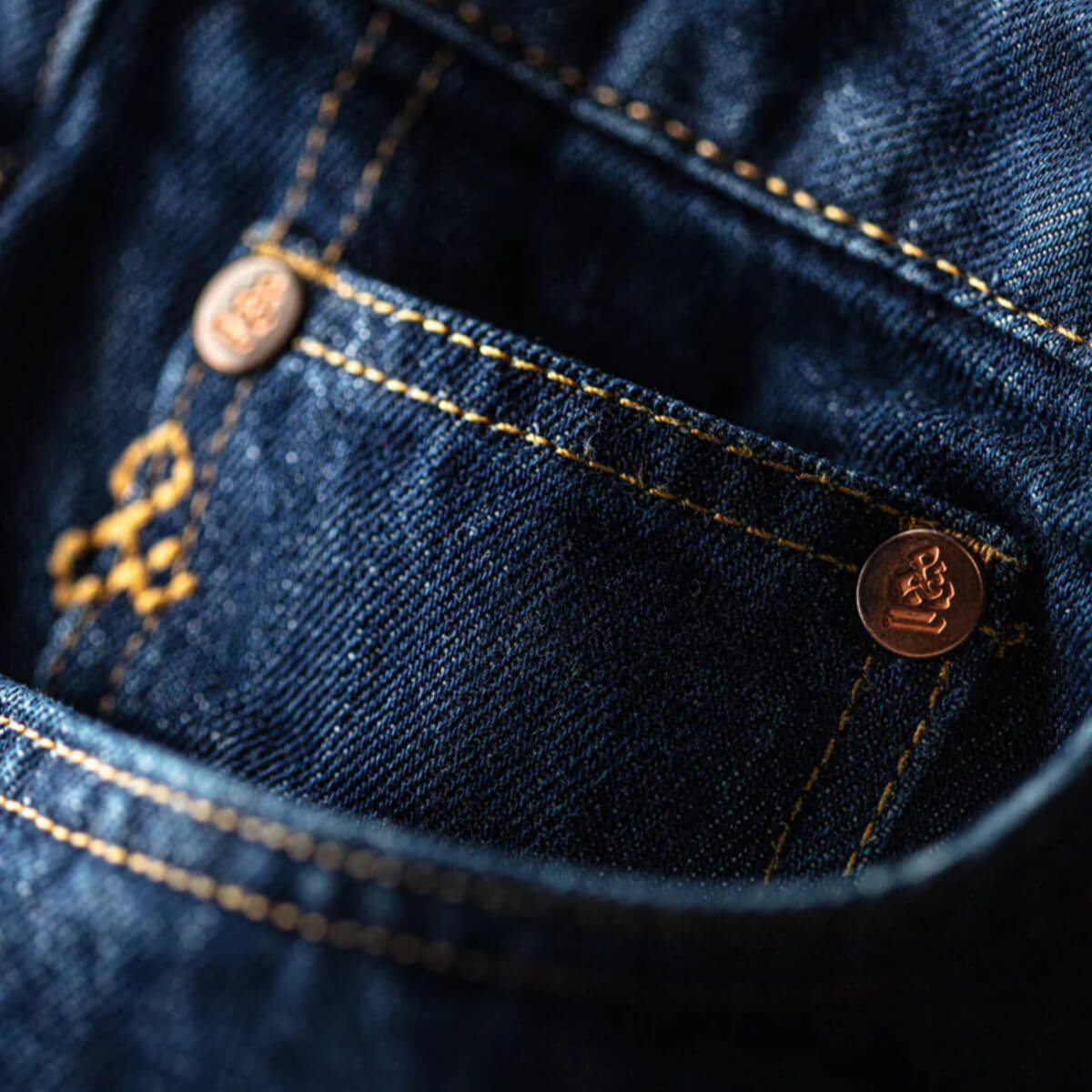 Close-up of blue denim fabric with gold stitching and buttons.