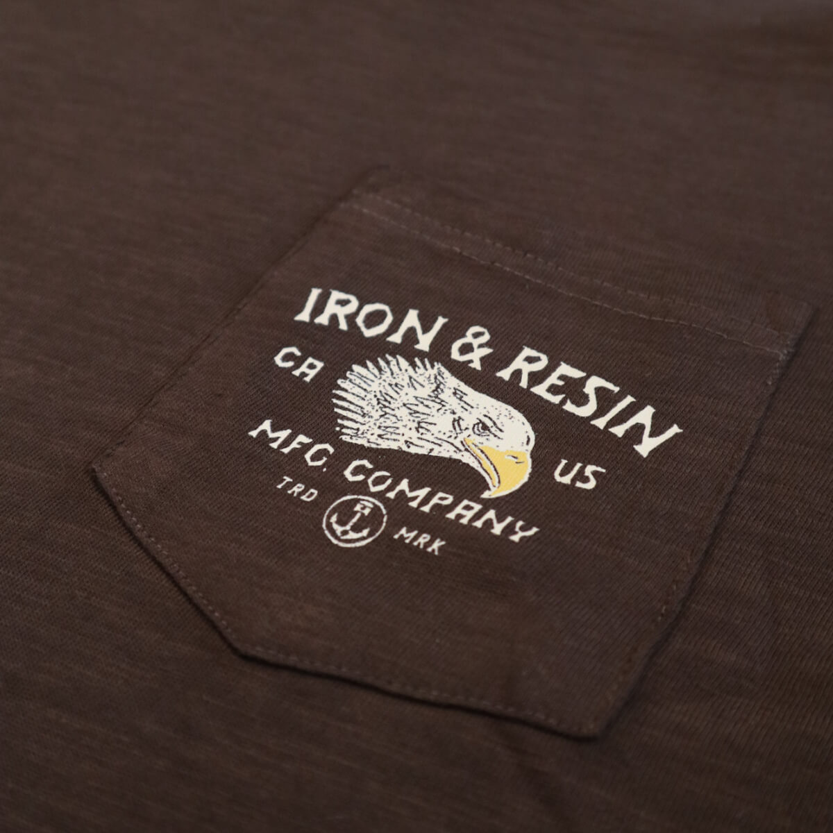 Close-up of a brown shirt with an embroidered logo on the chest pocket.