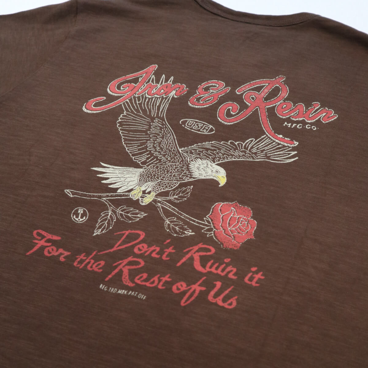 Brown t-shirt with eagle and rose graphic and text on a plain background
