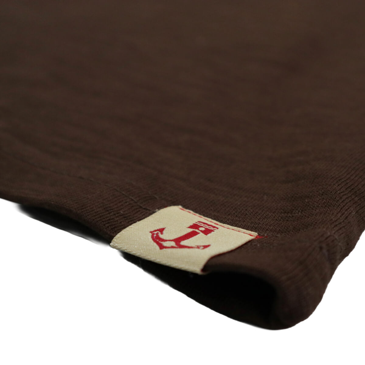 Close-up of a brown garment with a brand label featuring a red anchor on a white background