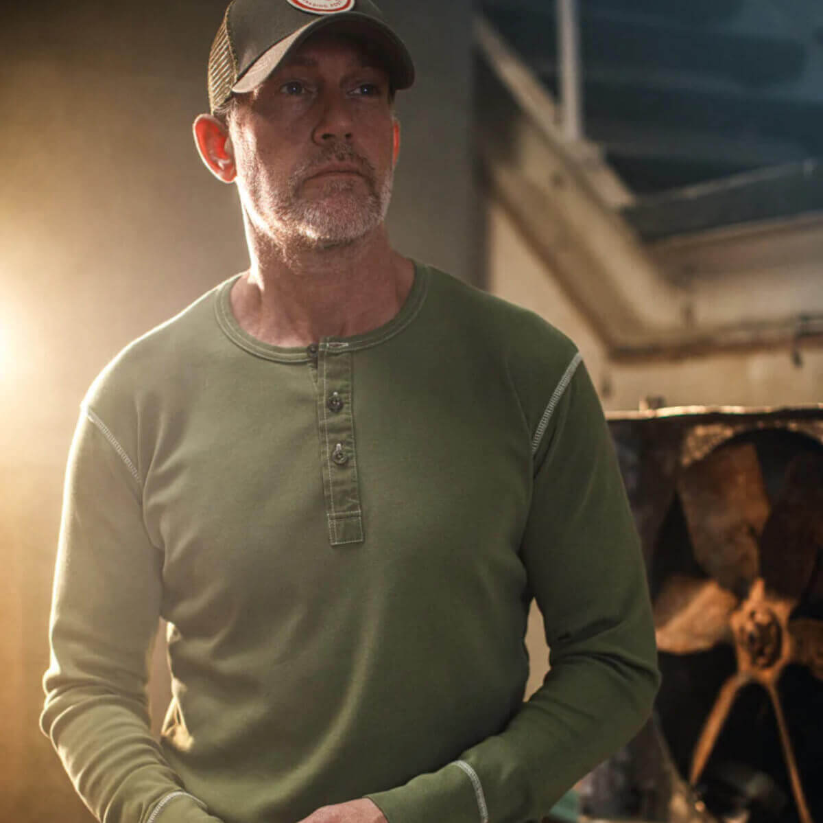 Man wearing a green long-sleeve shirt and cap standing in front of a vehicle.
