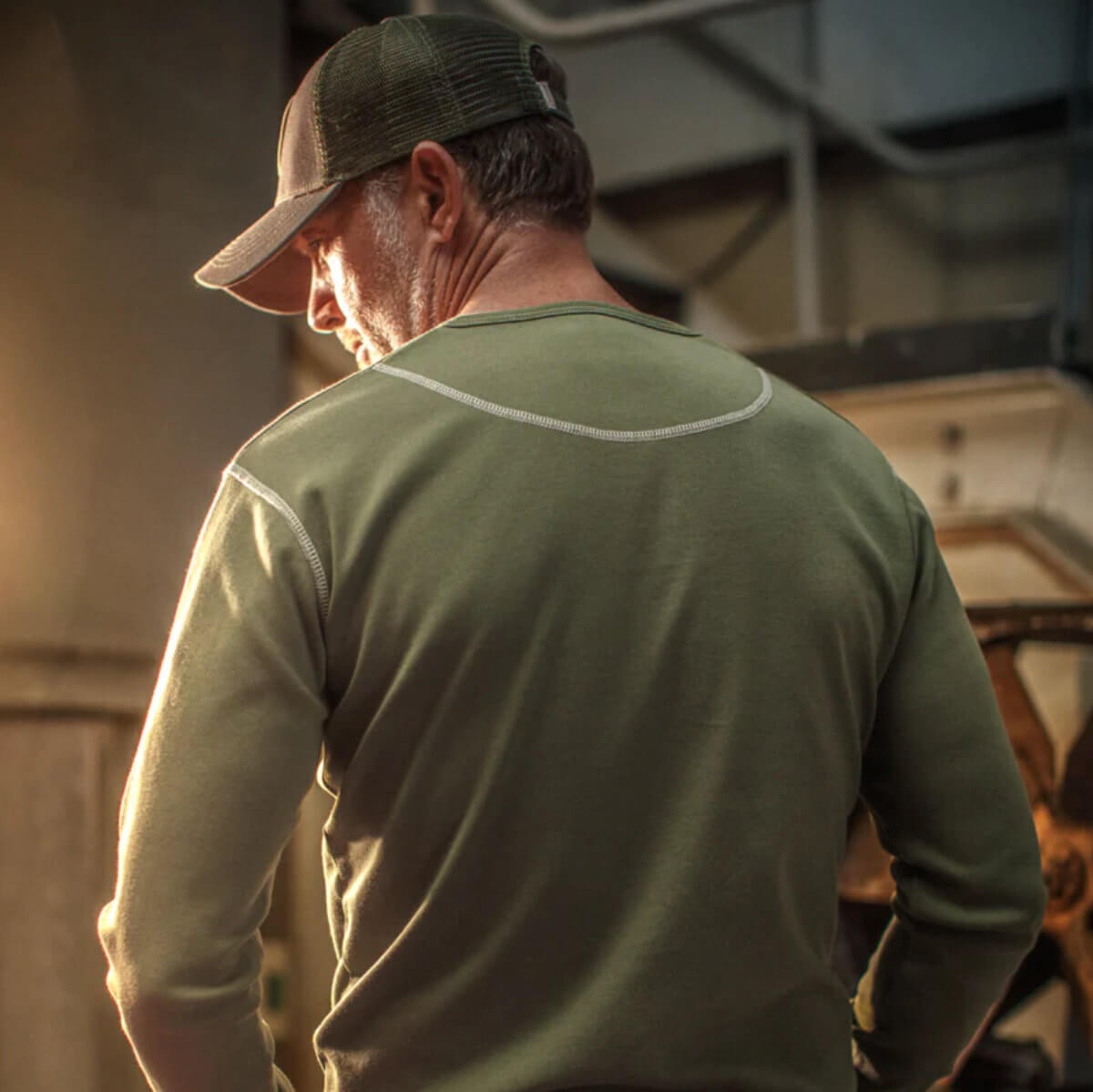 Man wearing a green cap and long-sleeve shirt in an industrial setting