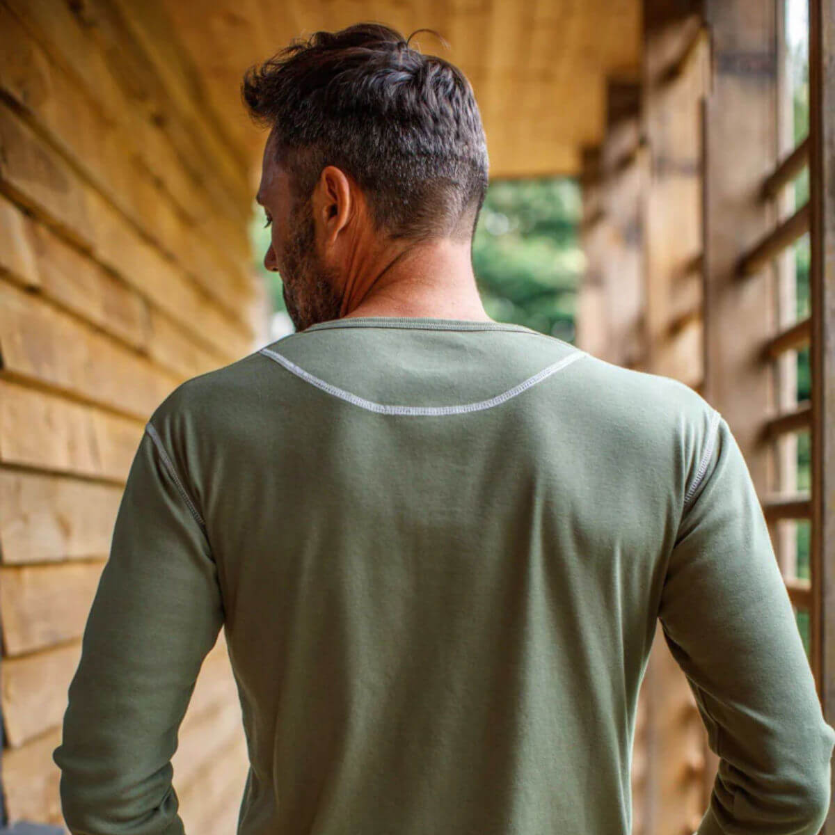 Man wearing a green long-sleeve shirt standing in front of a wooden structure.