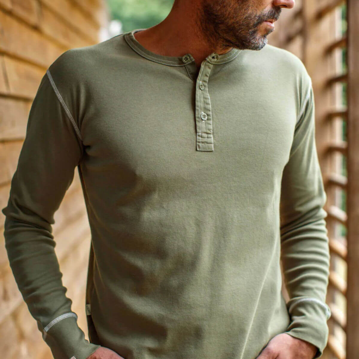 Man wearing a green long-sleeve henley shirt against a wooden background