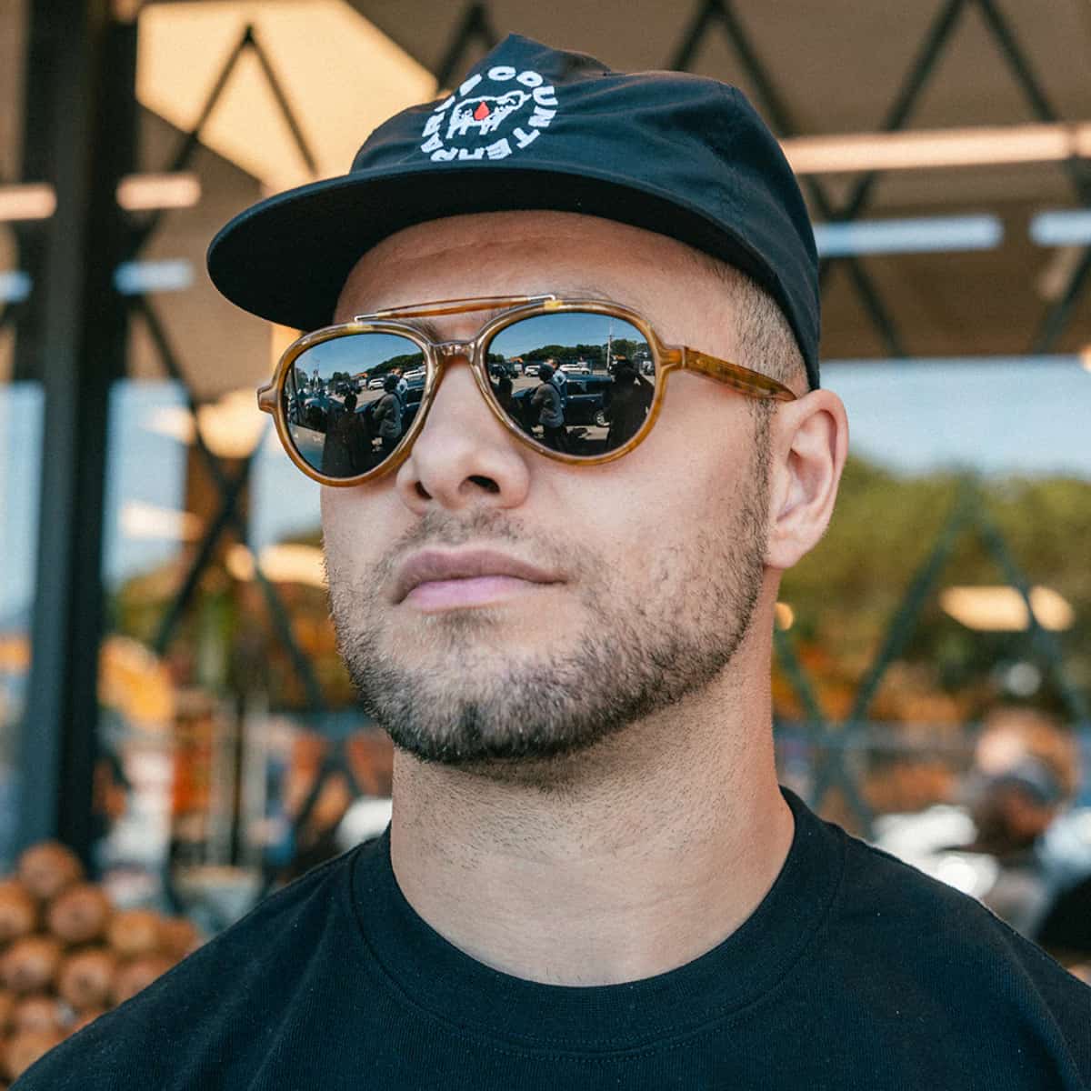 Man wearing a black cap and Vallon Elmore Brow Bar Sunglasses with a blurred background