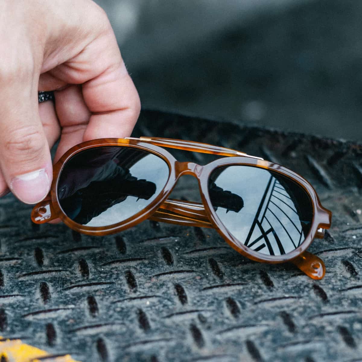 Vallon Elmore Brow Bar Sunglasses with reflective lenses held by a hand on a textured surface