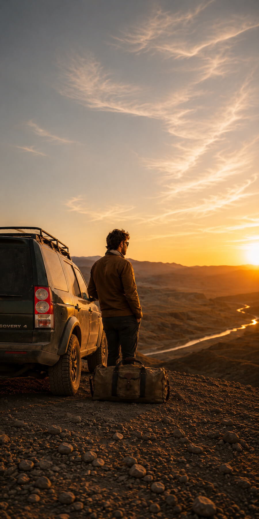 Man standing next to a Land Rover at sunset with mountains in the background