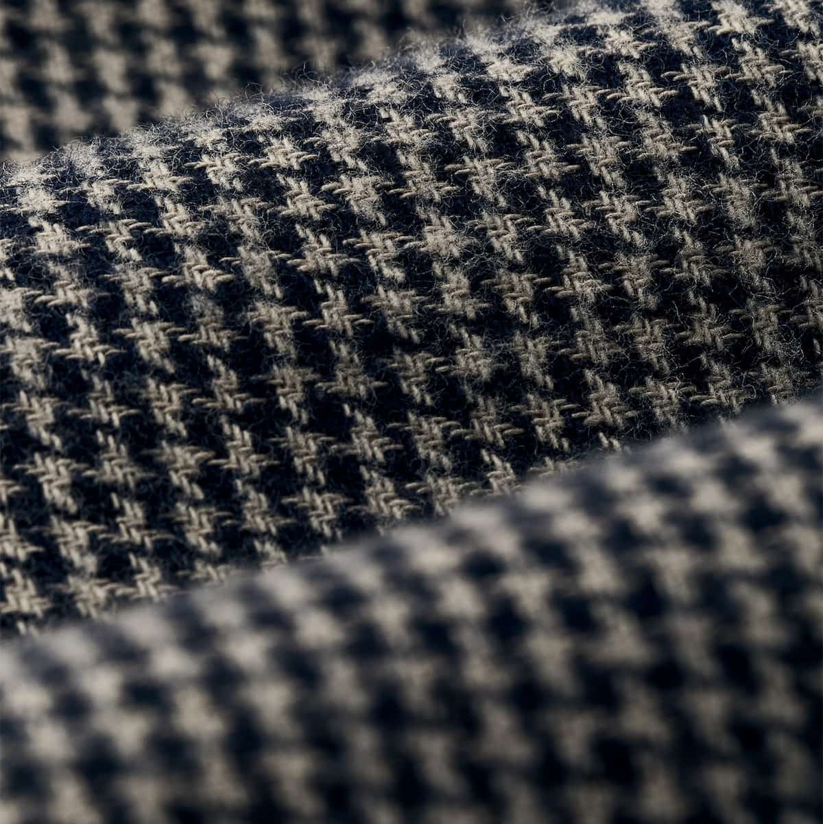 A close-up of a woven Filson fabric with a small-scale houndstooth pattern in dark navy and warm off-white.