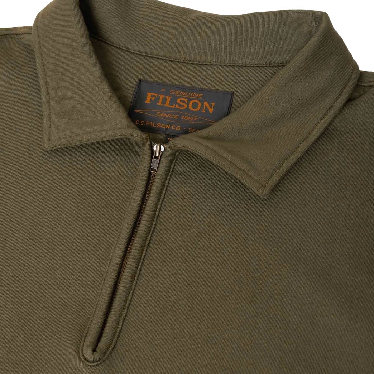 Close-up of a Filson quarter-zip polo shirt in olive green, showing the collar, zipper, and the black and orange brand label inside the neck.
