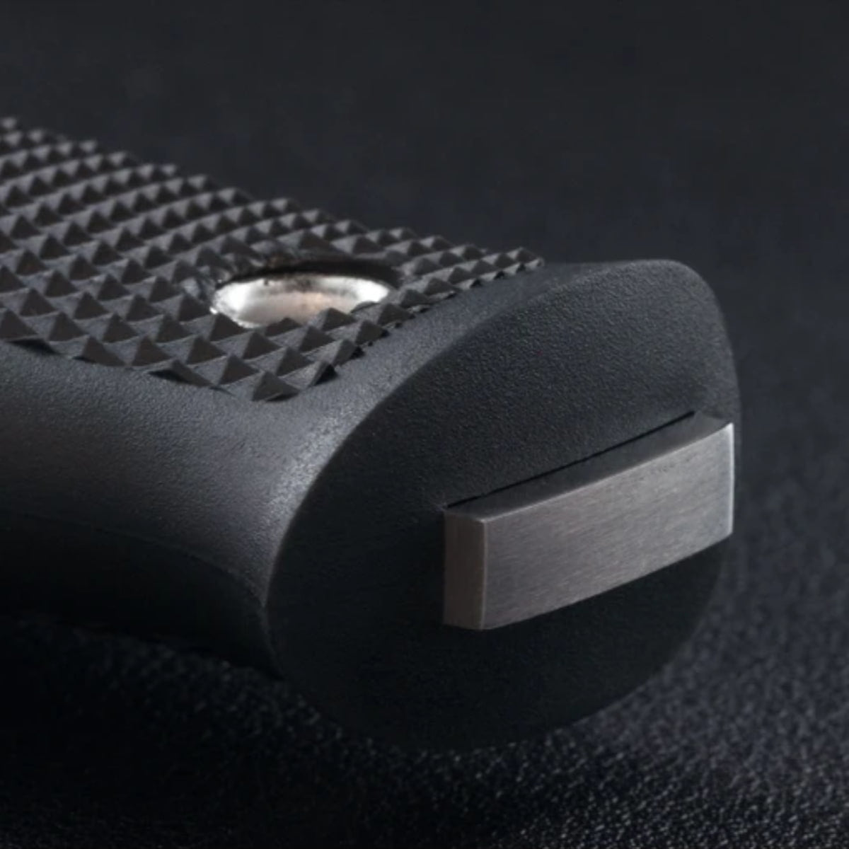 Close-up of a black textured handle with a brushed silver metal accent on a dark background.