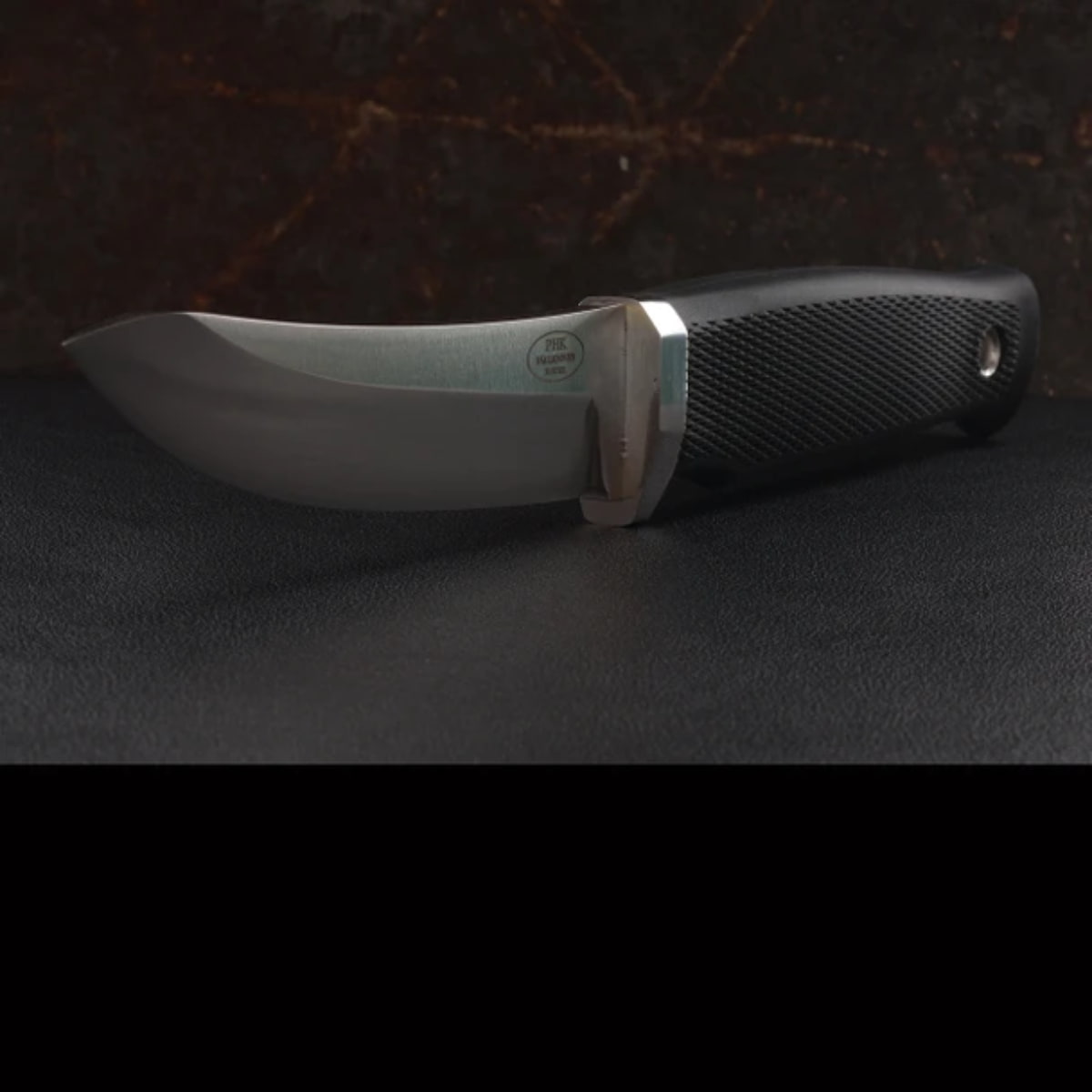 A fixed-blade knife with a curved silver steel blade and a textured black handle, resting on a dark textured surface.