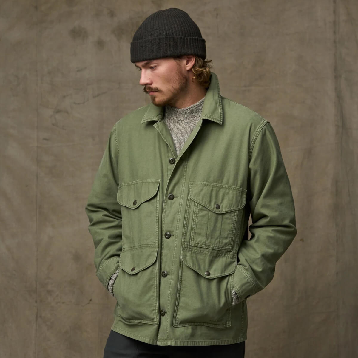 Man wearing a green jacket and black beanie against a brown background