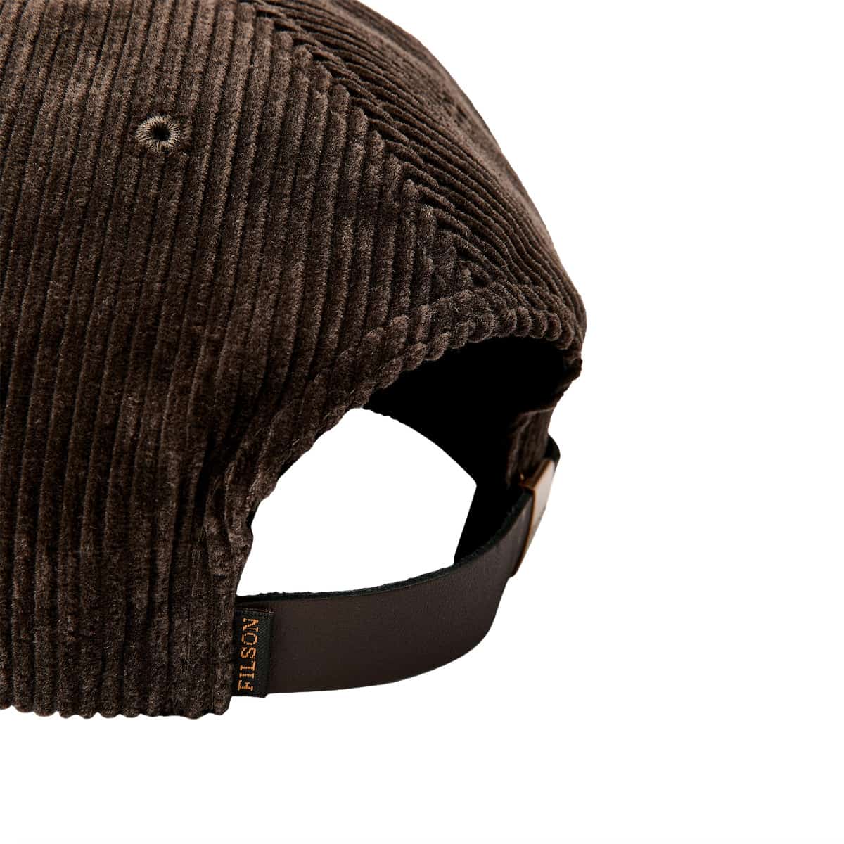 Close-up of a brown Filson corduroy cap showing the textured fabric, eyelet, and black adjustable strap with a small FILSON tag.