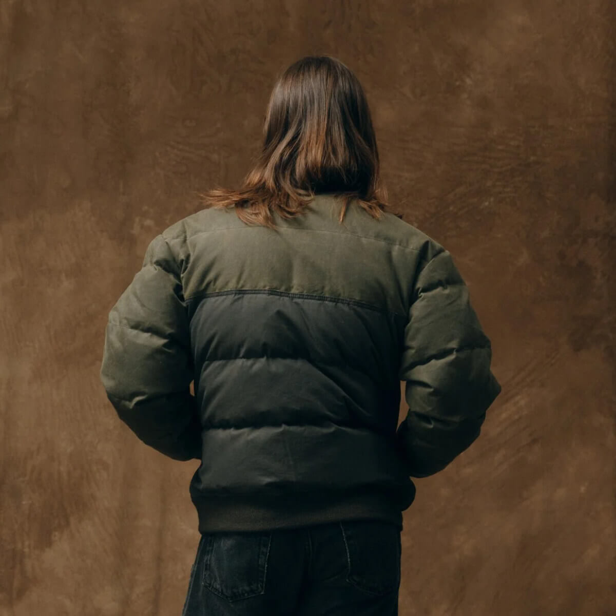 Person wearing a green bomber jacket against a brown textured background