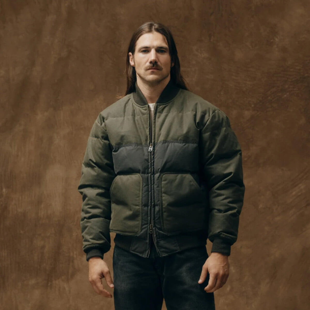 Man wearing a green puffer jacket against a brown background
