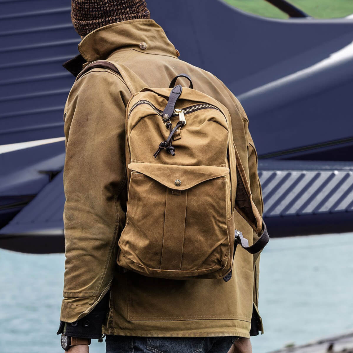 Person wearing a brown jacket and carrying a matching brown backpack with a blurred background.