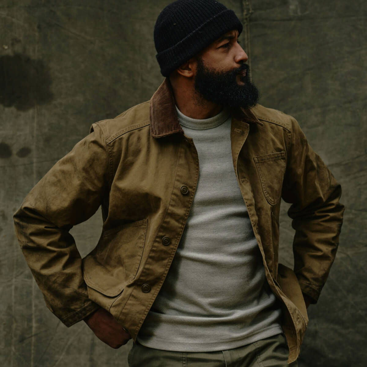 Man wearing a brown jacket and black beanie against a textured green background