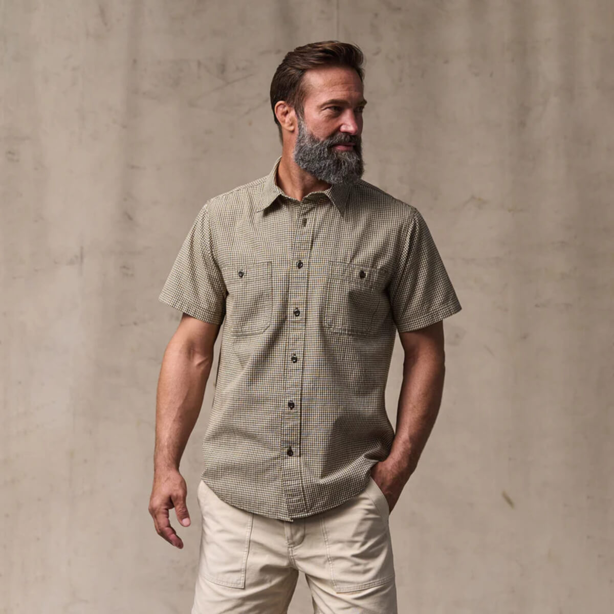 Man wearing a green checkered shirt and beige pants against a beige background