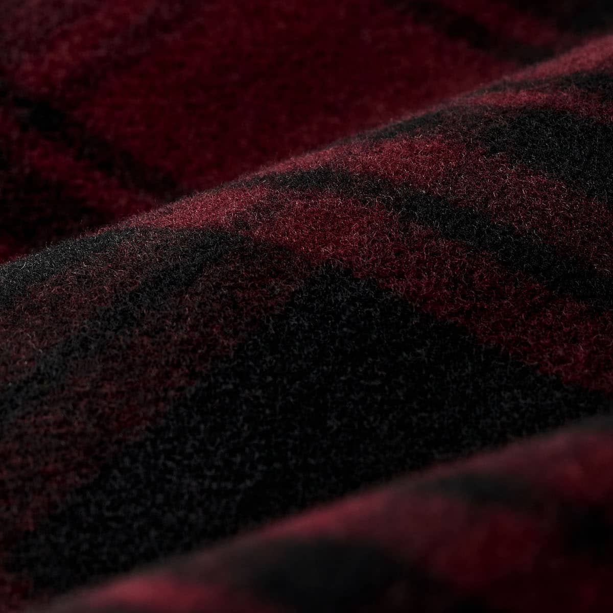 A close-up of a soft, plush fabric with a deep red and black plaid pattern.