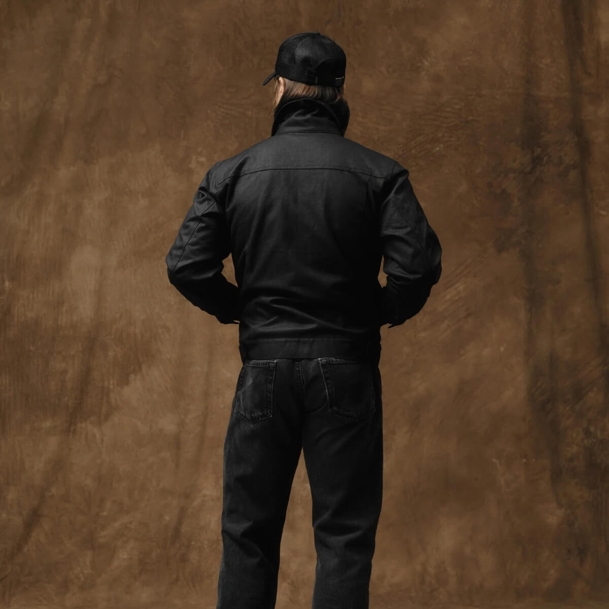 Person wearing a black jacket and cap against a brown textured background