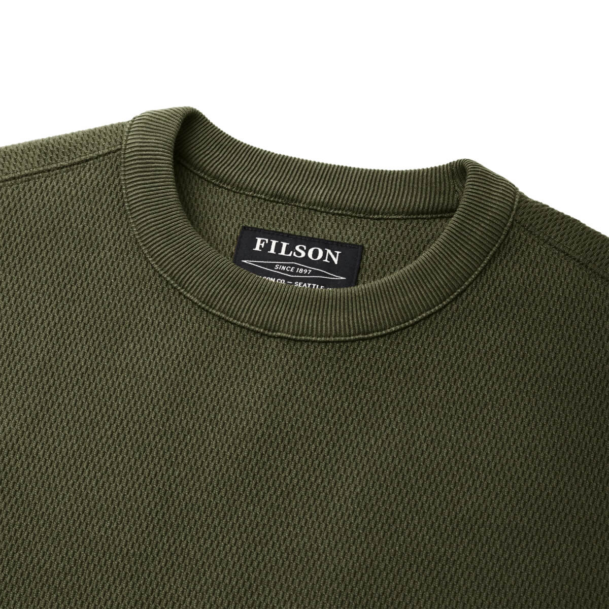 Close-up of a green sweater with a Filson label on a white background