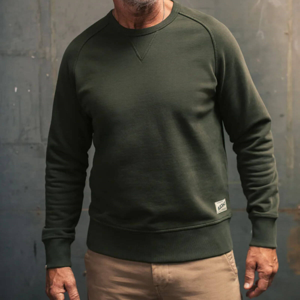 Person wearing a green sweatshirt with a &amp;SONS logo against a grey background