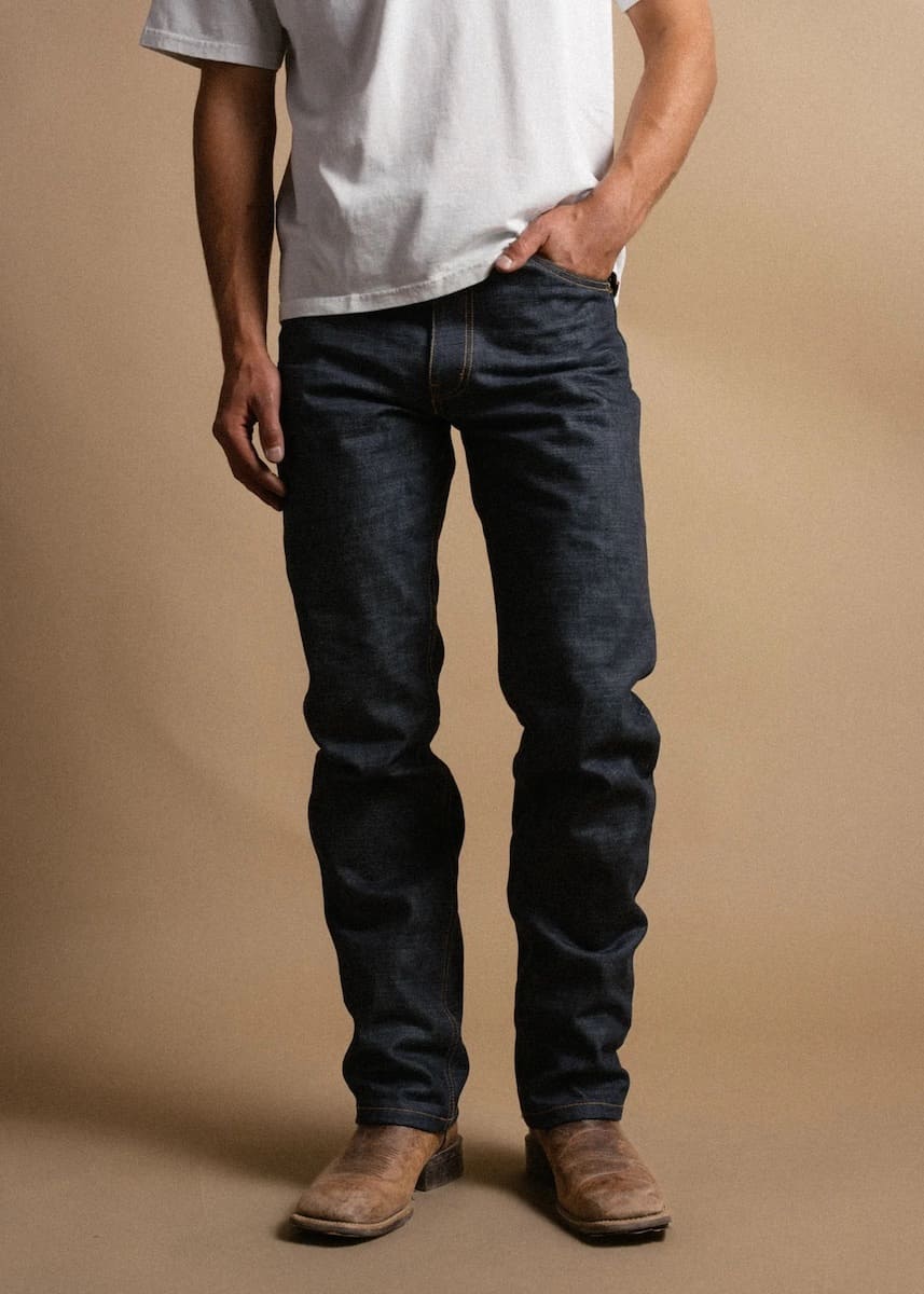 Person wearing dark rider jeans and a white shirt against a beige background