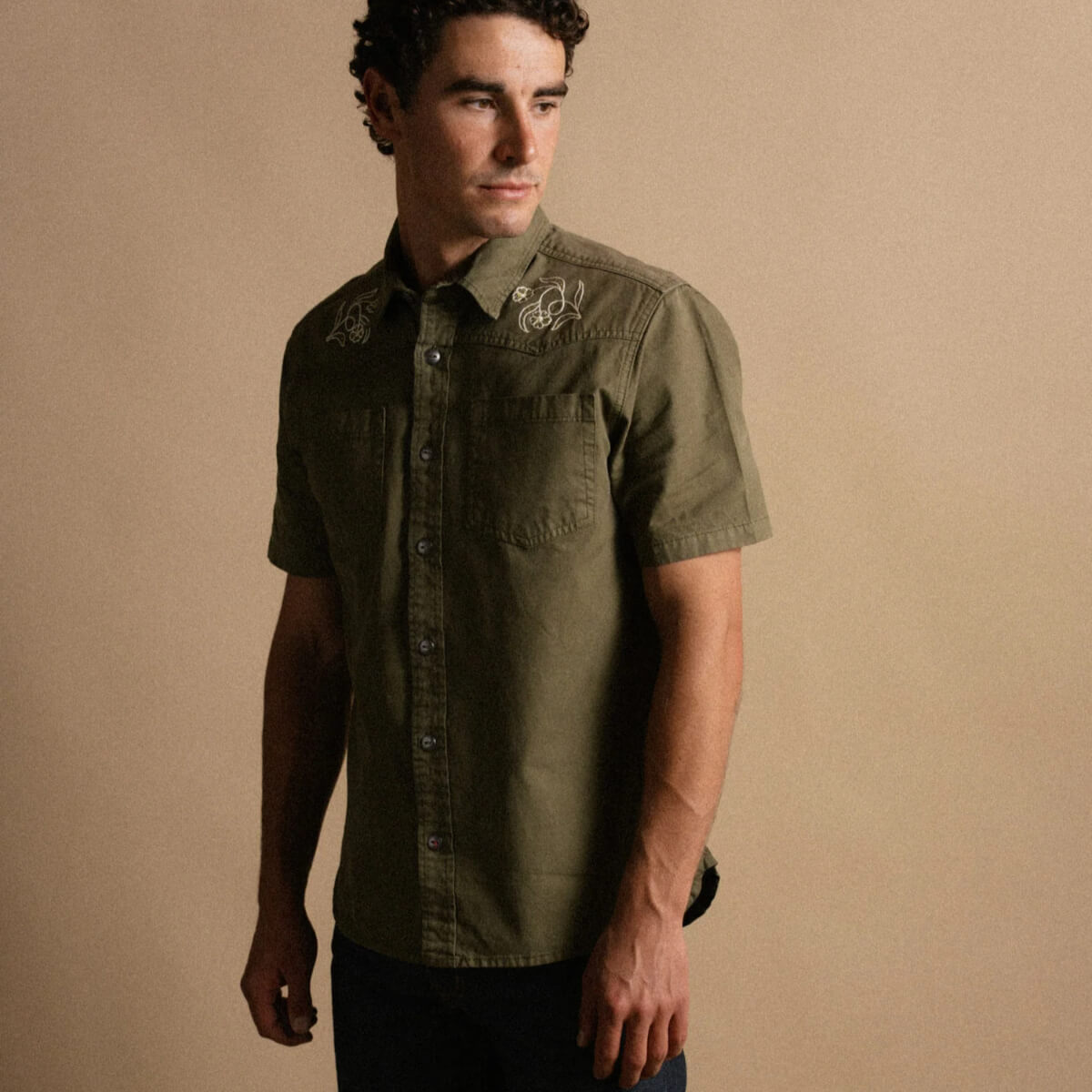 Man wearing a green short-sleeve shirt with embroidery on a beige background